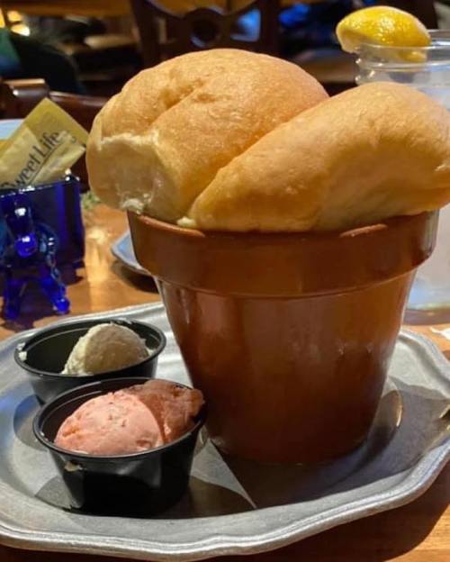 A clay pot filled with two fluffy bread rolls, accompanied by two small cups of ice cream in different flavors.