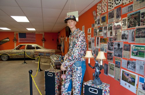 A colorful display featuring a mannequin in a beaded outfit, a decorated car, and a wall of newspaper clippings.