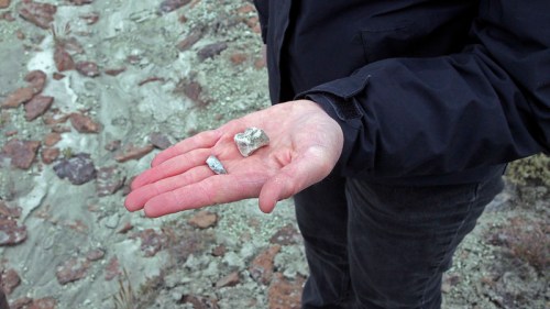 A hand holding two small rocks against a rocky, textured background.