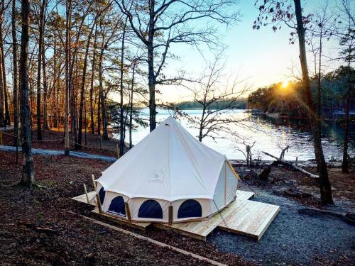 A glamping tent on a wooden platform by a lake, surrounded by trees at sunset.