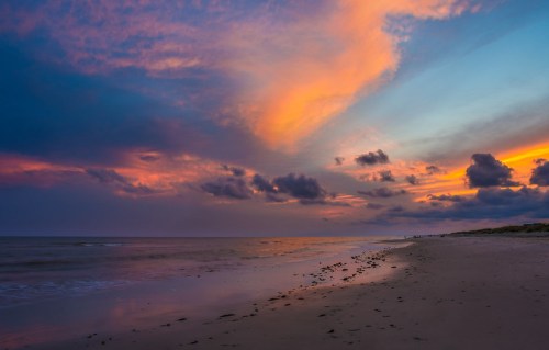 A serene beach at sunset, with vibrant clouds and colorful skies reflecting over calm waters.