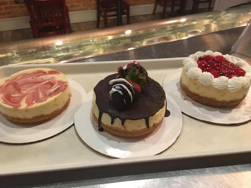 Three mini cheesecakes on a tray: strawberry swirl, chocolate-covered with a strawberry, and cherry-topped.