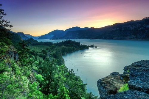 A serene landscape of a river winding through mountains at sunset, with lush greenery and a calm sky.