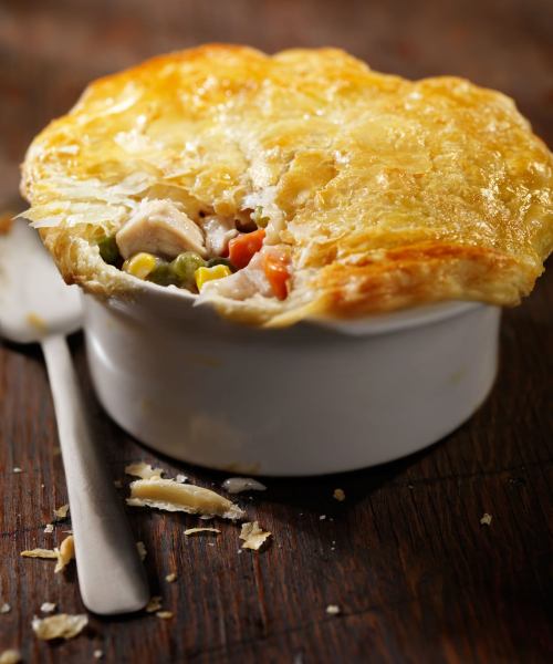 A golden-brown chicken pot pie with a flaky crust, partially opened to reveal filling of chicken and vegetables.