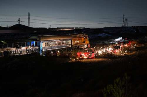 A train at night, surrounded by lights and equipment, with workers and machinery near the tracks.