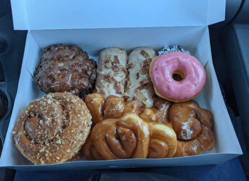 A box of assorted donuts and pastries, including glazed, pink-frosted, and cinnamon rolls, arranged neatly.