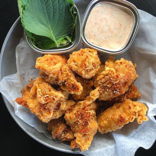 A platter of crispy fried chicken pieces with a side of dipping sauce and fresh greens.