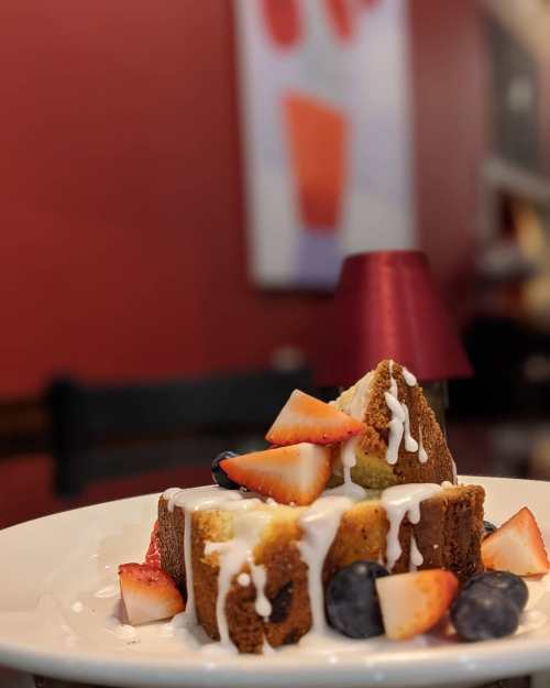 A slice of cake topped with strawberries and blueberries, drizzled with white icing, on a white plate.