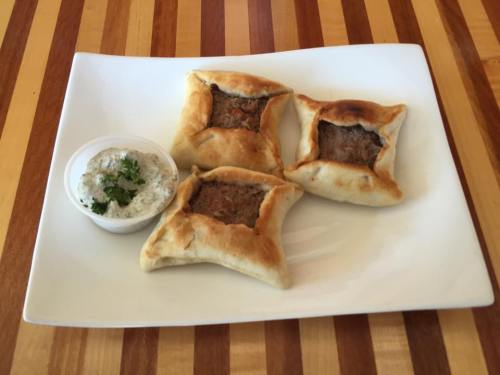 Three golden-brown stuffed pastries on a white plate, accompanied by a small bowl of dipping sauce.
