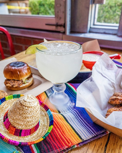 A refreshing margarita with lime, a mini sombrero, and a spread of delicious food on a colorful table setting.
