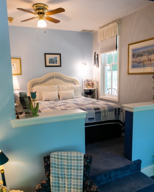 Cozy bedroom with a blue color scheme, a wicker headboard, and a ceiling fan, featuring soft lighting and decorative art.