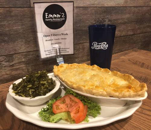 A plate with a golden pie, a side of greens, and a tomato slice, next to a Pepsi cup and a restaurant sign.