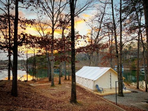A white tent by a lake surrounded by trees, with a sunset casting warm colors in the sky.