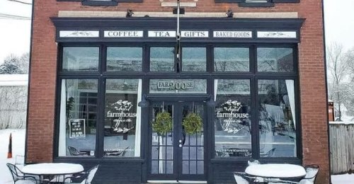 A cozy storefront featuring "Coffee, Tea, Gifts, Baked Goods" signs, with winter decor and outdoor seating.