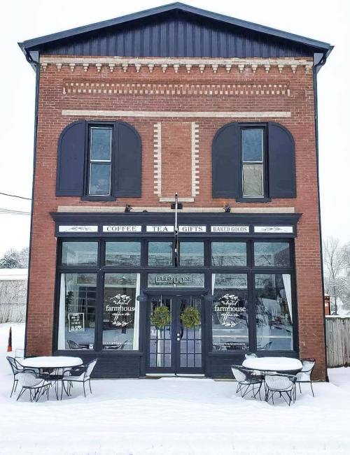 A charming brick coffee shop with large windows, snow-covered outdoor seating, and festive wreaths on the doors.