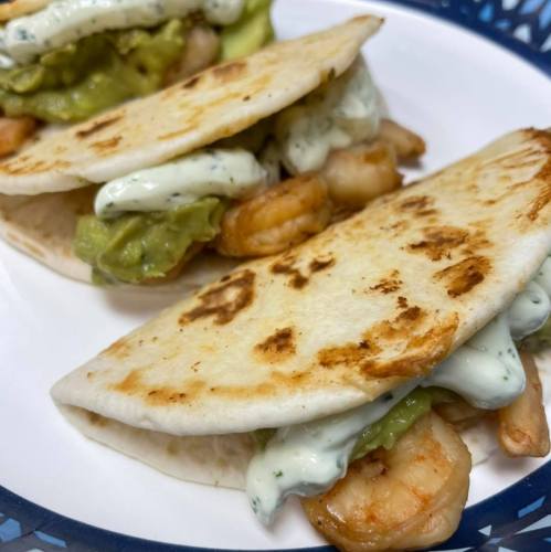 Two tortillas filled with shrimp, guacamole, and a creamy sauce, served on a white plate.