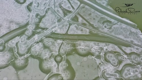 Aerial view of frozen water with intricate ice patterns and bubbles, creating a textured, abstract landscape.