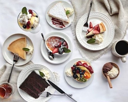 A variety of desserts on plates, including cakes, fruit, and ice cream, arranged on a table with a coffee cup.