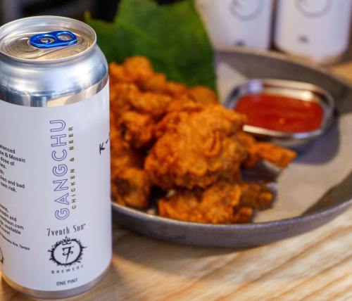 A plate of crispy fried chicken with a can of beer and a small dish of dipping sauce on a wooden table.