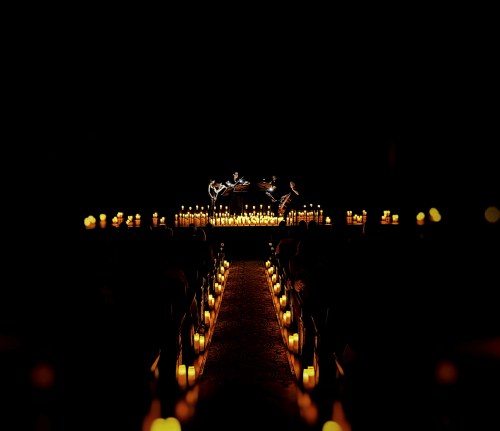 A dimly lit venue with rows of candles lining a pathway leading to a beautifully decorated stage.