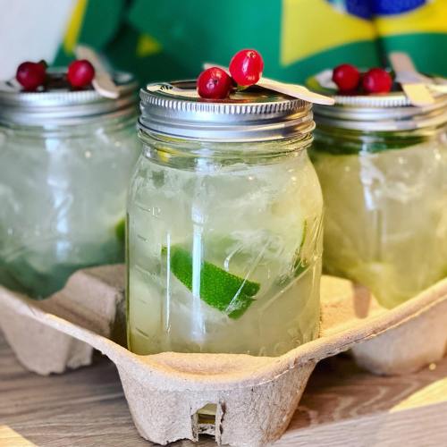 Three mason jars filled with a refreshing drink, garnished with lime and cranberries, on a cardboard tray.
