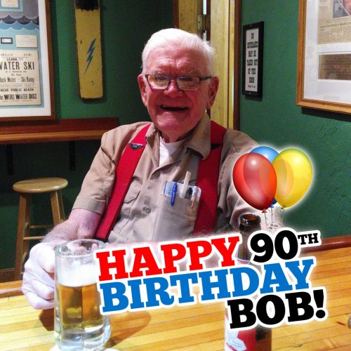 An elderly man with glasses smiles at a table, holding a beer, with a "Happy 90th Birthday Bob!" message and balloons.