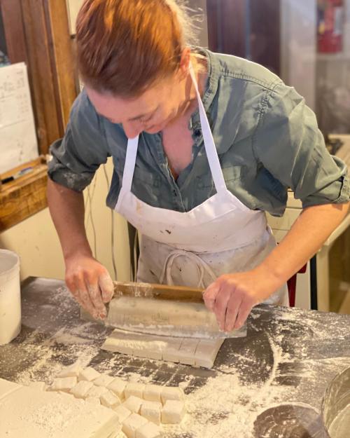 A person in an apron rolls out dough on a floured surface, focused on their task in a cozy kitchen setting.