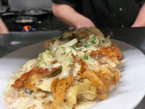 A close-up of a plated dish featuring crispy fried chicken topped with creamy sauce and green onions.