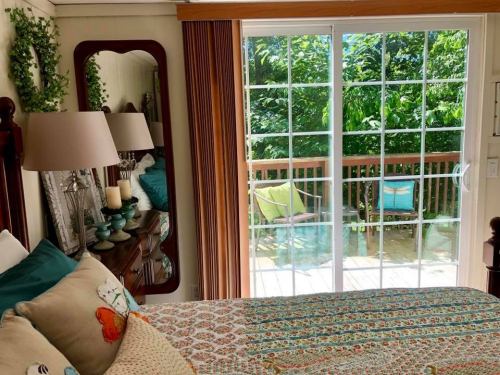Cozy bedroom with a patterned bedspread, mirror, lamps, and sliding glass doors leading to a deck with greenery outside.