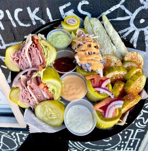 A platter of pickles filled with deli meats, accompanied by various dipping sauces and sliced vegetables.