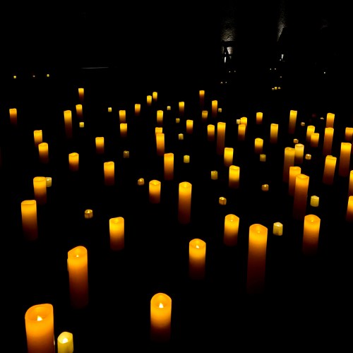 A dark space filled with numerous glowing yellow candles, creating a warm and serene atmosphere.