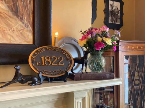 A decorative mantel display featuring a plaque, flowers in a vase, and small figurines.