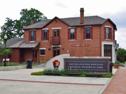 Historic brick building with a sign for Dayton Aviation Heritage National Historical Park, surrounded by greenery.