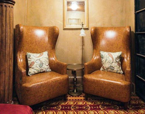Two vintage leather armchairs with decorative pillows, a small side table, and a mirror in a cozy, warmly lit room.