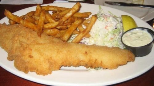 A plate featuring a fried fish fillet, French fries, coleslaw, a lemon wedge, and a small cup of tartar sauce.