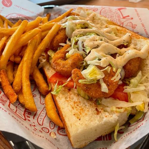 A sandwich with fried shrimp, lettuce, and tomato, served with a side of golden French fries.