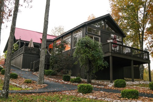 A modern black house with a red roof, surrounded by trees and landscaped shrubs, on a scenic hillside.