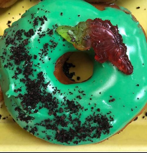 A green frosted donut topped with crushed cookies and a gummy worm.