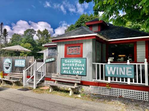 A quaint restaurant with a red and gray exterior, featuring signs for beer, wine, and all-day breakfast and lunch.