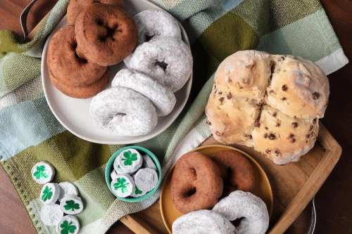 Two plates of donuts—chocolate and powdered sugar—on a checkered cloth, with shamrock candies in a small bowl.