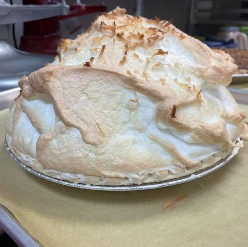 A fluffy coconut meringue pie with a golden-brown toasted topping, sitting on a baking sheet.