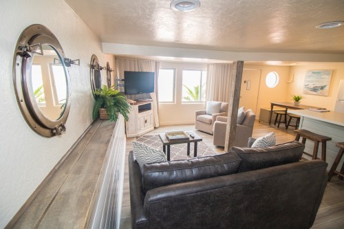 Cozy living room with modern decor, large windows, and a view of palm trees. Features a sofa, chairs, and a TV.