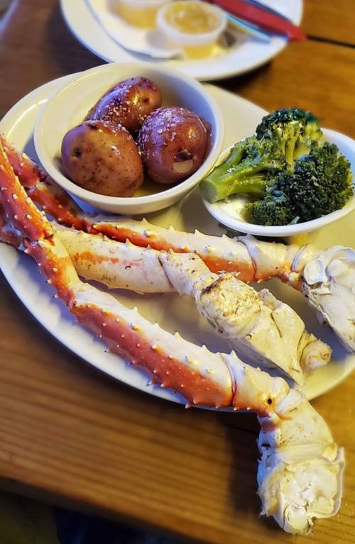 A plate with two large crab legs, boiled potatoes, and steamed broccoli.