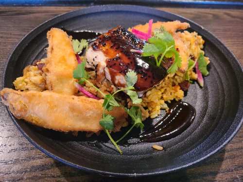 A plate of grilled chicken with a glossy sauce, served on a bed of rice and garnished with herbs and colorful vegetables.