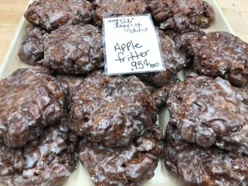 A tray of glazed apple fritters with a sign indicating they cost $0.95 each.