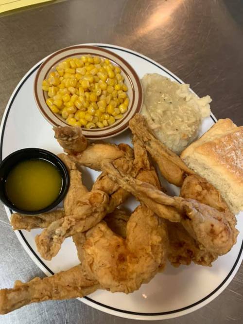 A plate of fried frog legs, corn, rice, and a biscuit with a side of melted butter.
