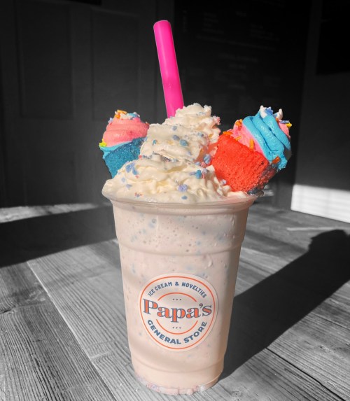 A milkshake topped with whipped cream, colorful sprinkles, and two mini cupcakes, served in a cup from Papa's General Store.