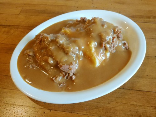 A plate of meatloaf covered in brown gravy, served on a wooden table.