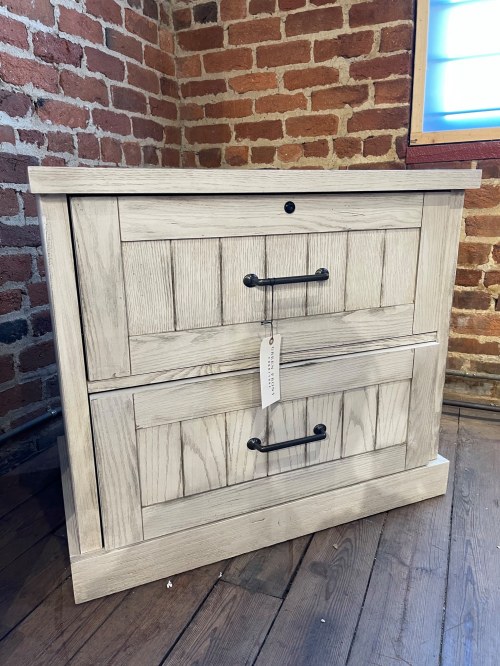 A rustic wooden dresser with two drawers and black metal handles, set against a brick wall.