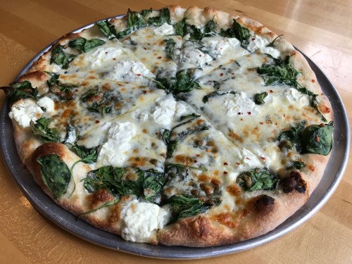 A freshly baked pizza topped with spinach, dollops of ricotta cheese, and melted mozzarella on a golden crust.